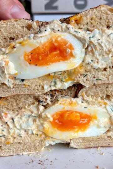chopped egg salad everything bagel with a soft boiled egg in the middle