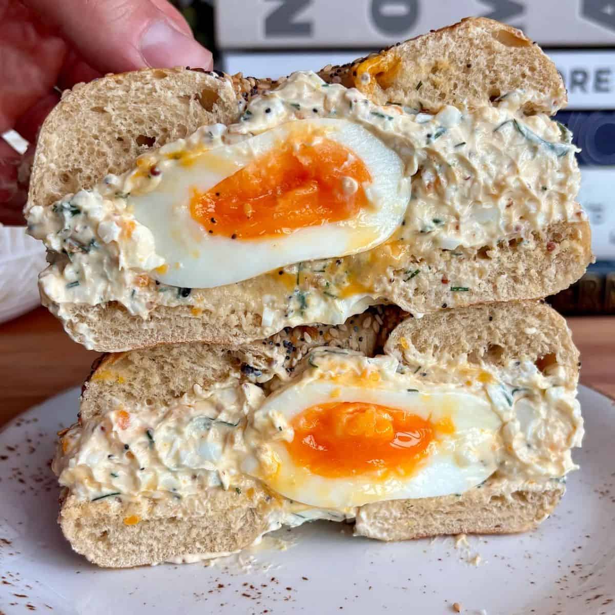 chopped egg salad everything bagel with a soft boiled egg in the middle
