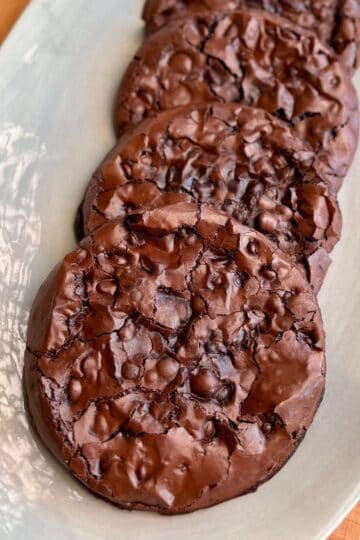 plate of crispy crackly chewy brownie cookies with shiny chocolatey tops and chocolate chips