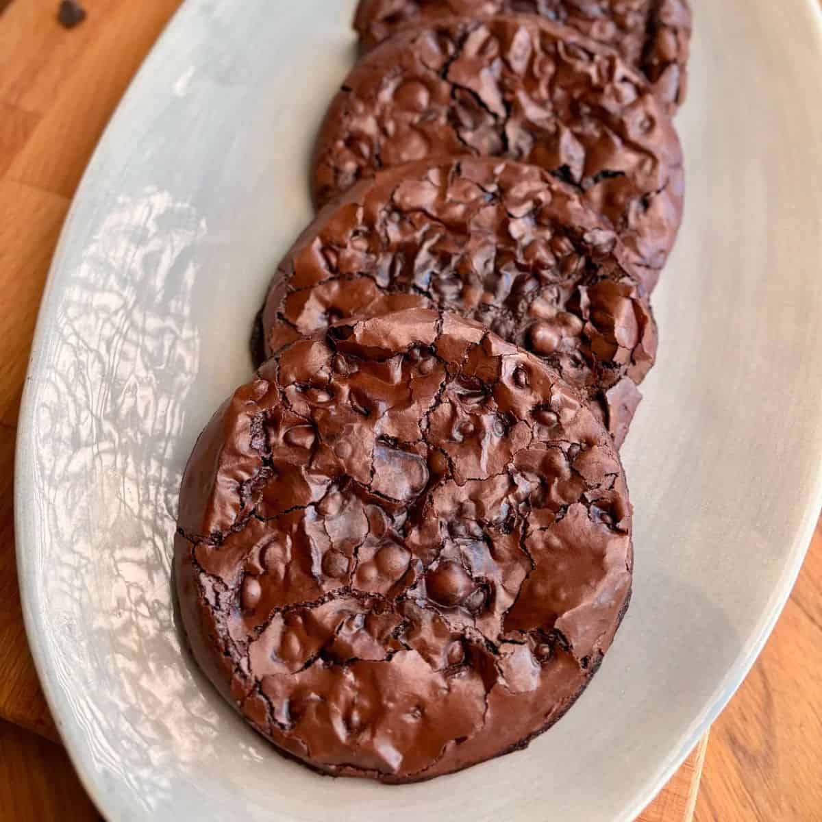 plate of crispy crackly chewy brownie cookies with shiny chocolatey tops and chocolate chips