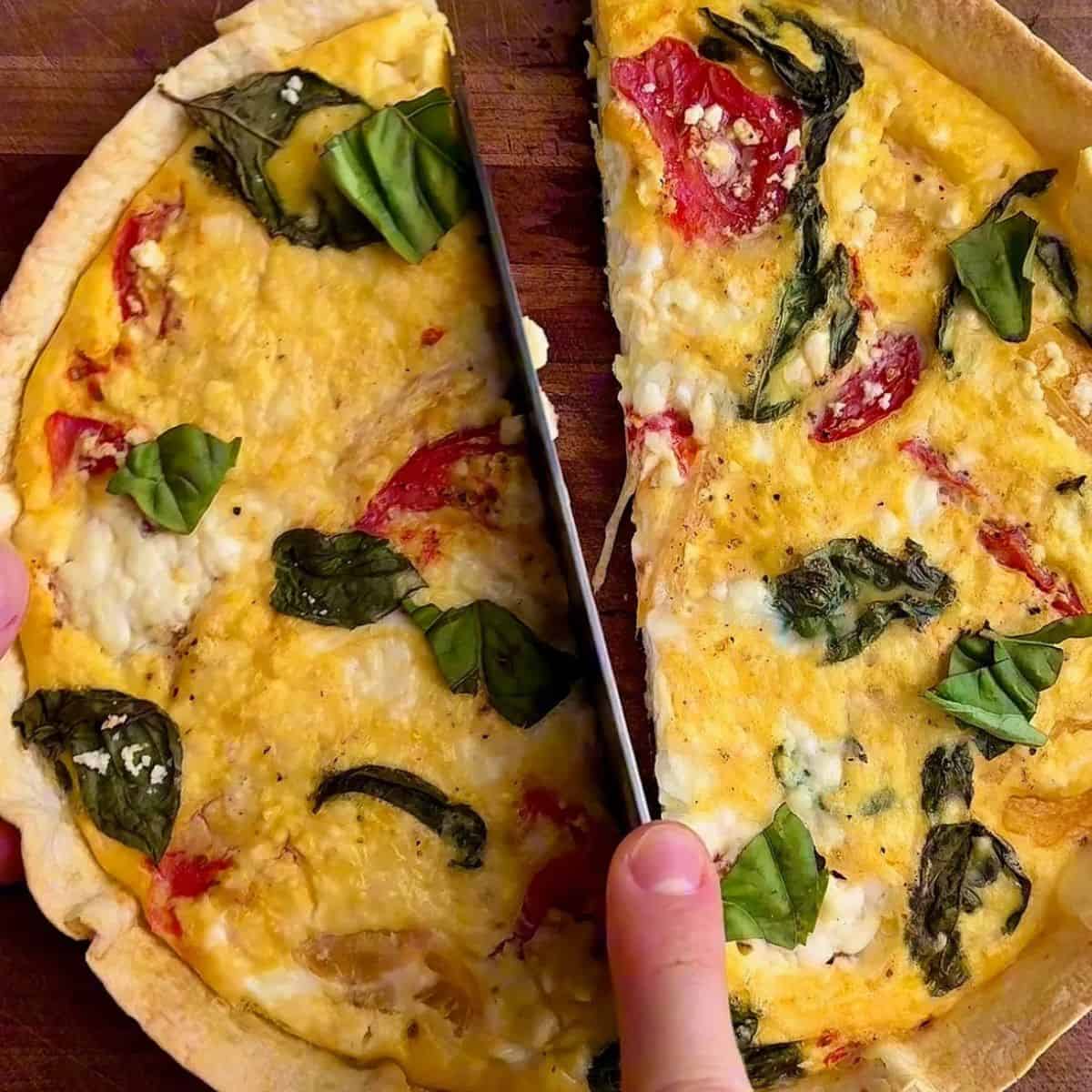 easy high protein tortilla quiche sliced in half and topped with roasted tomatoes, feta, and fresh basil