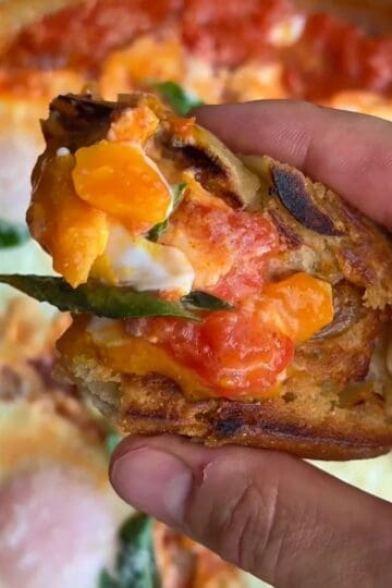 eggs in purgatory with tomato, eggs and basil on top of a crusty, toasted baguette