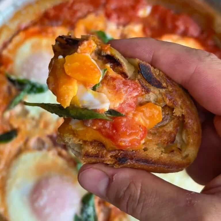 eggs in purgatory with tomato, eggs and basil on top of a crusty, toasted baguette