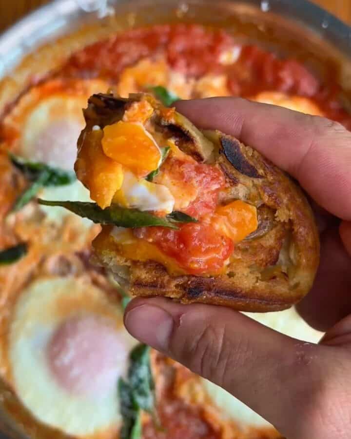 bite of eggs in purgatory with runny egg and tomato, topped with fresh basil