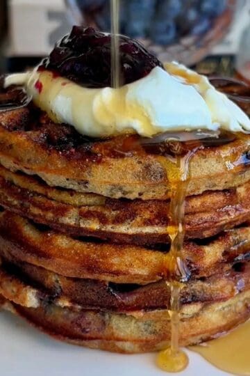 stack of healthy blueberry mini waffles topped with yogurt, fresh blueberries and maple syrup drizzle