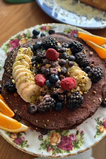 Healthy chocolate protein pancakes with fresh berries, chopped pistachios and orange slices