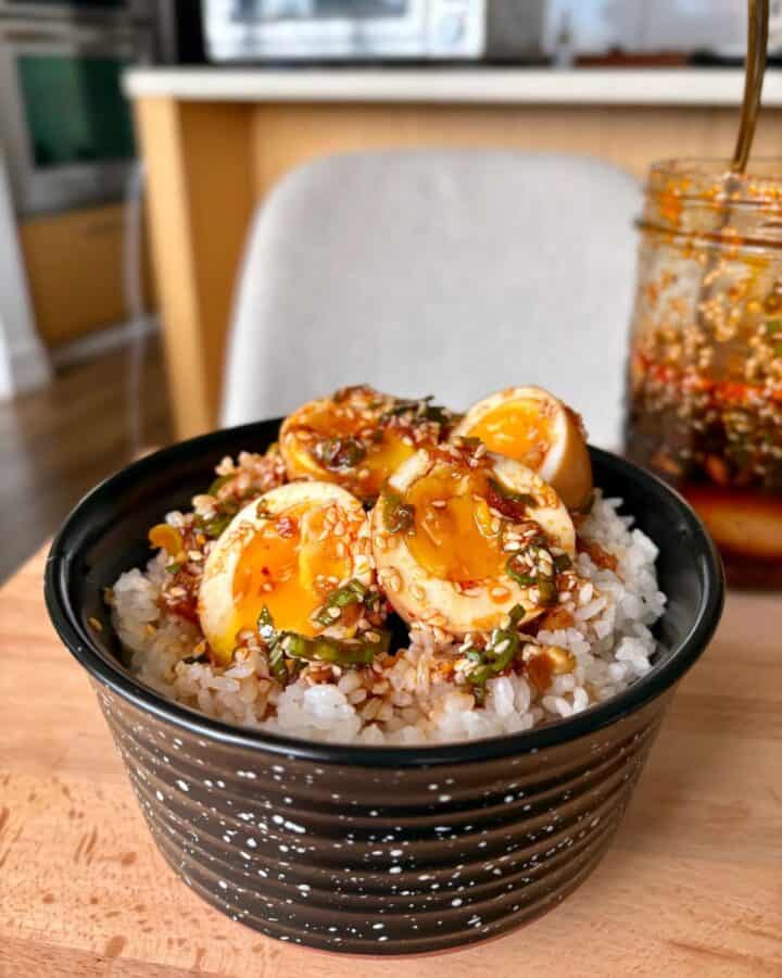 Bowl of korean marinated eggs with jasmine rice topped with sesame seeds and green onion