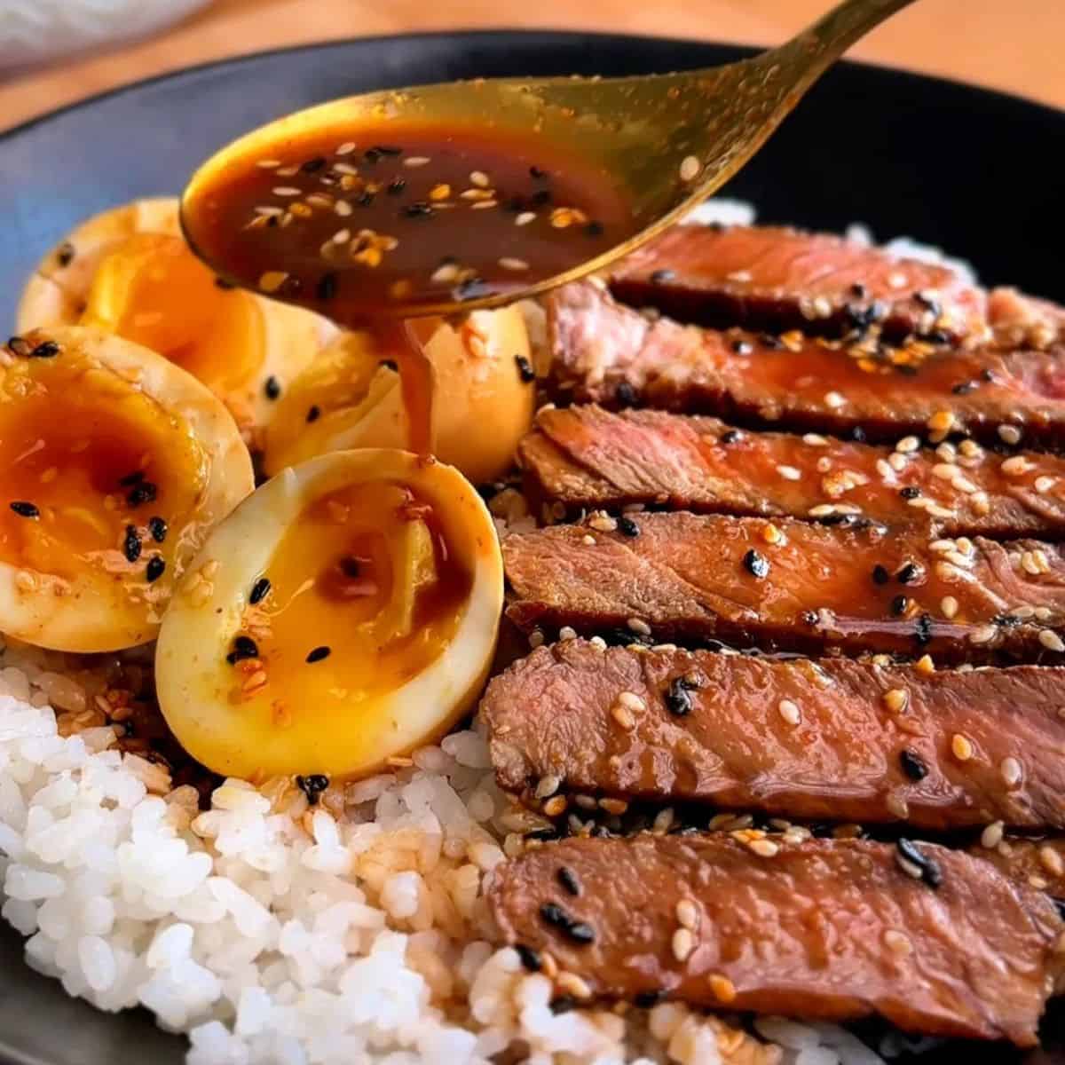 miso soy sesame steak with eggs over rice, sprinkled with black and white sesame seeds
