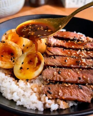 miso soy sesame steak, topped with sesame seeds, with eggs over a bed of white rice