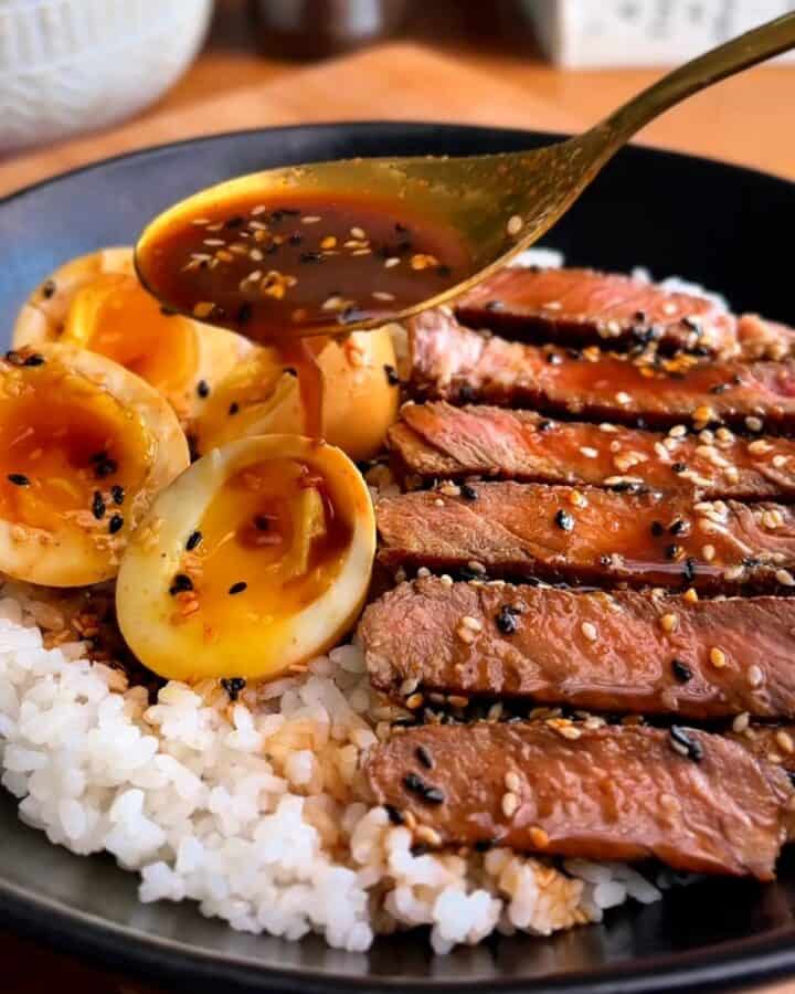 miso soy sesame steak, topped with sesame seeds, with eggs over a bed of white rice