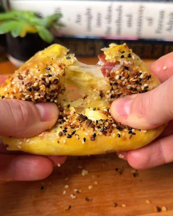 hands pulling apart a bacon, egg and cheese rice paper bagel with everything bagel seasoning