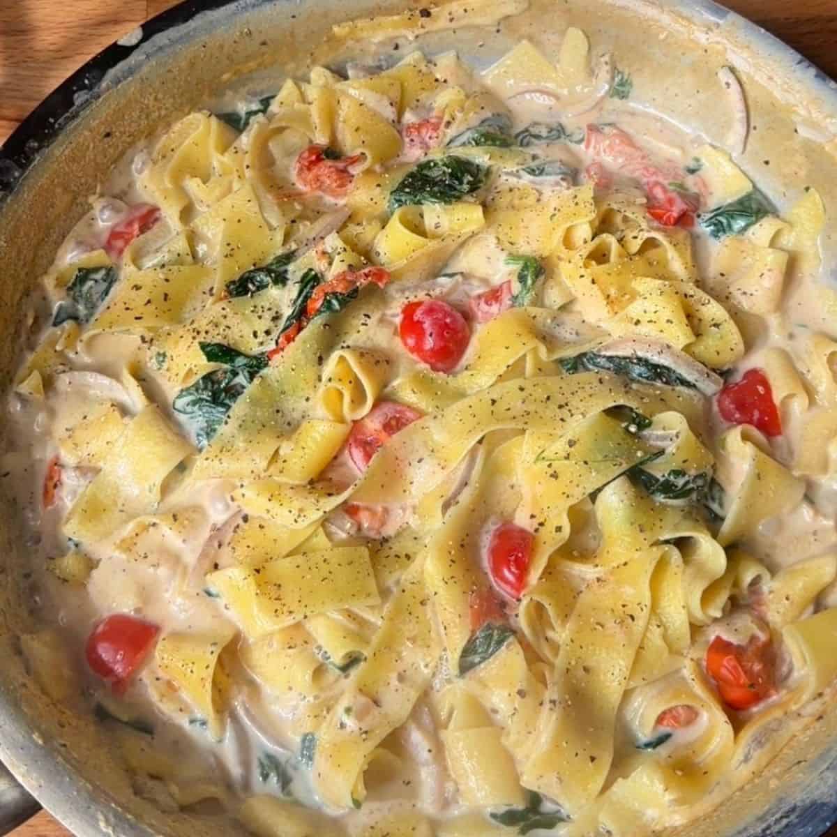 creamy one pan tomato and spinach fettuccine in a pan, sprinkled with black pepper