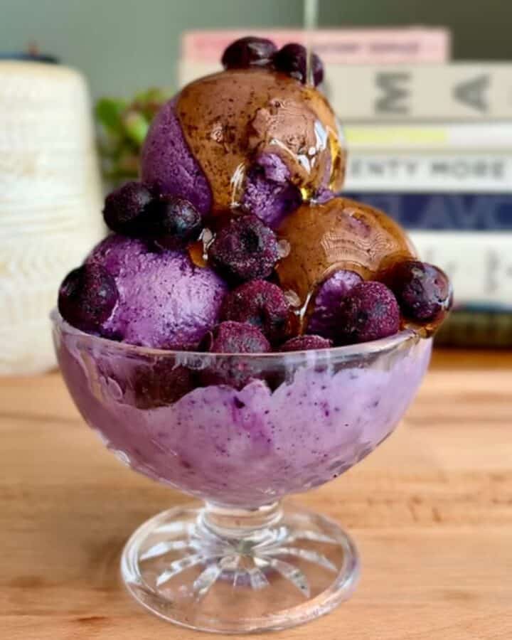 healthy protein packed blueberry ice cream sundae with frozen blueberries and maple syrup drizzle