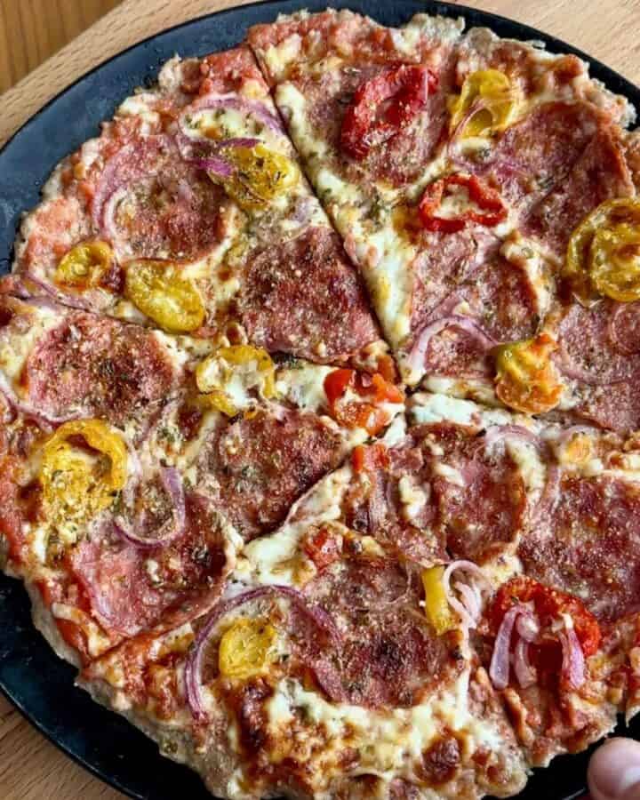 a round, crispy hot honey chicken crust pizza on a plate, topped with hot peppers, pepperoni, and red onion and melty cheese