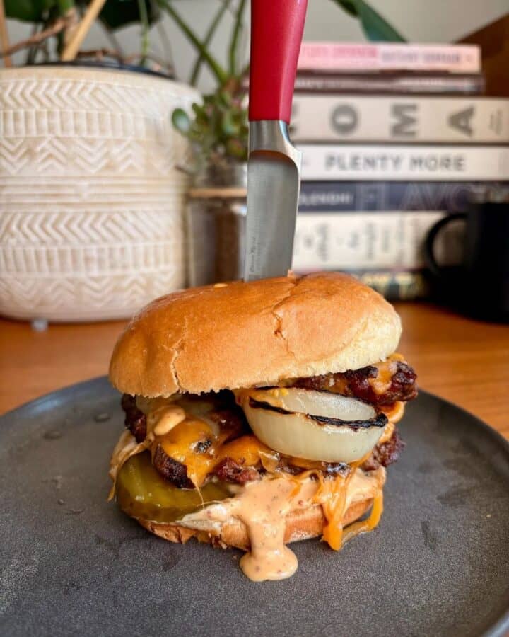 a juicy french onion burger with melted cheese and a dripping burger sauce, on a brioche bun with a knife decoratively stabbed through the center