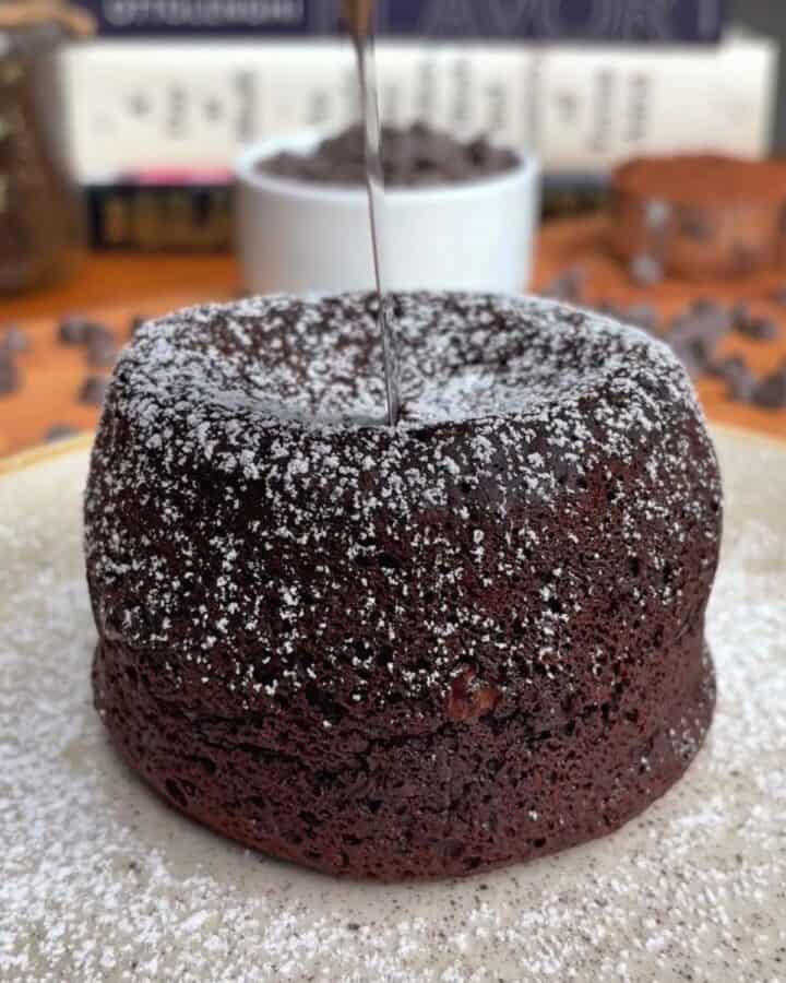 a round, oven baked chocolate lava cake on a plate, sprinkled in powdered sugar, waiting to be cut open