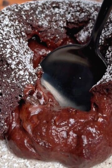 a spoon splicing open an oven baked chocolate lava cake sprinkled in powdered sugar