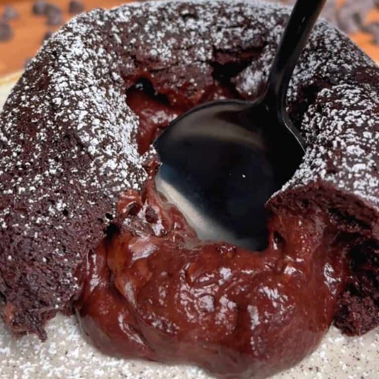 a spoon splicing open an oven baked chocolate lava cake sprinkled in powdered sugar