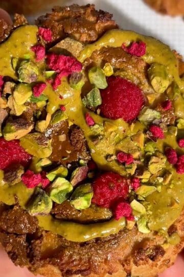 pistachio raspberry bun with golden brown edges, topped with pistachio butter swirl, fresh raspberries and chopped pistachios