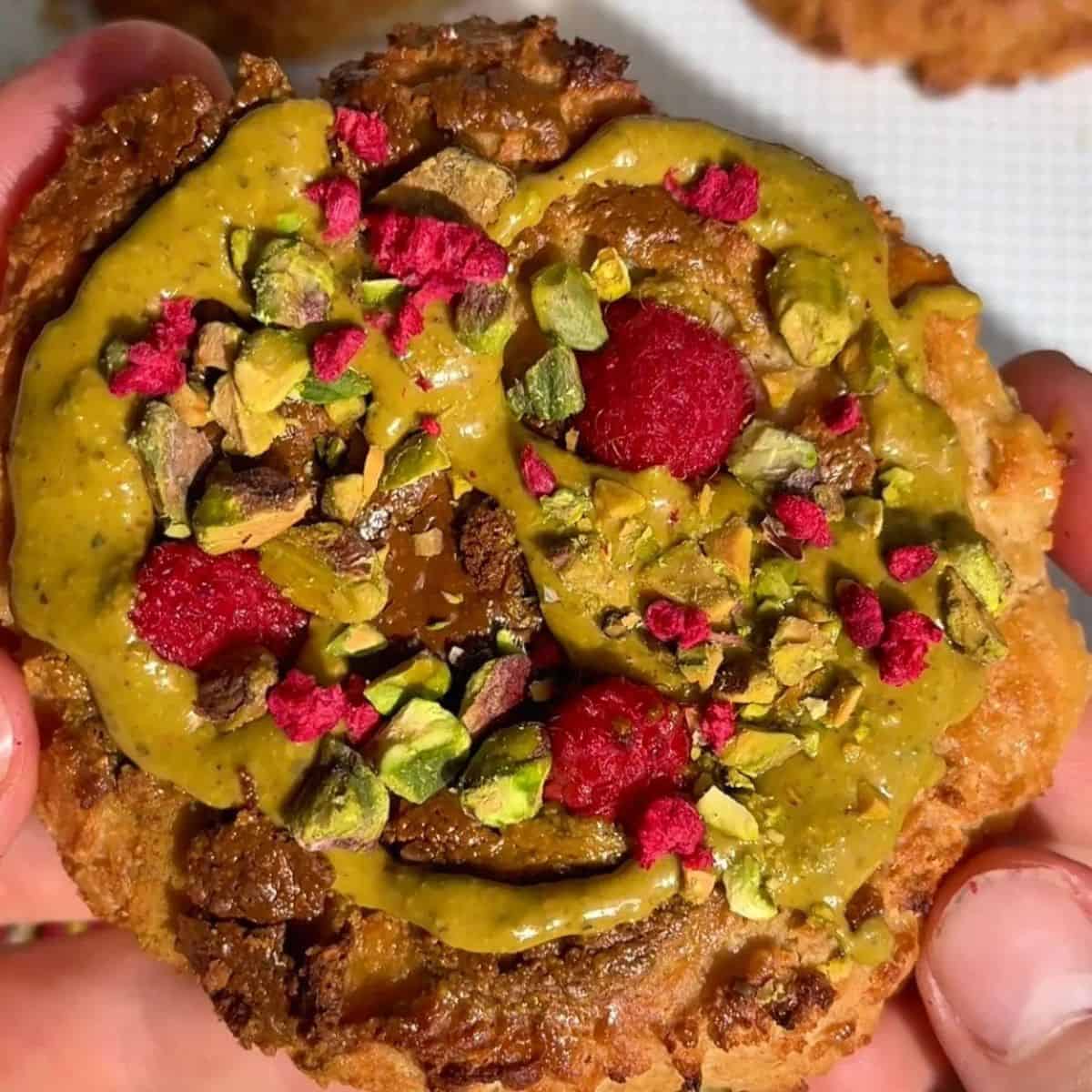 pistachio raspberry bun with golden brown edges, topped with pistachio butter swirl, fresh raspberries and chopped pistachios