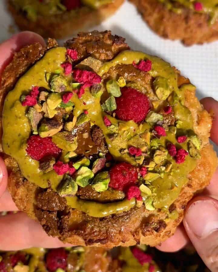 golden brown pistachio raspberry breakfast bun topped with pistachio butter swirl, fresh raspberries and chopped pistachios