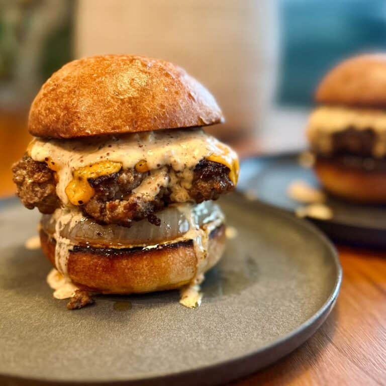 thick, juicy burger sitting on a plate, atop a crispy caramelized onion, sandwiched between two toasted buns and dripping in punchy burger sauce