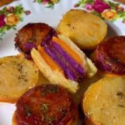 plate of tri-color sweet potato stacks made of white, orange and purple sweet potatoes, topped with rosemary