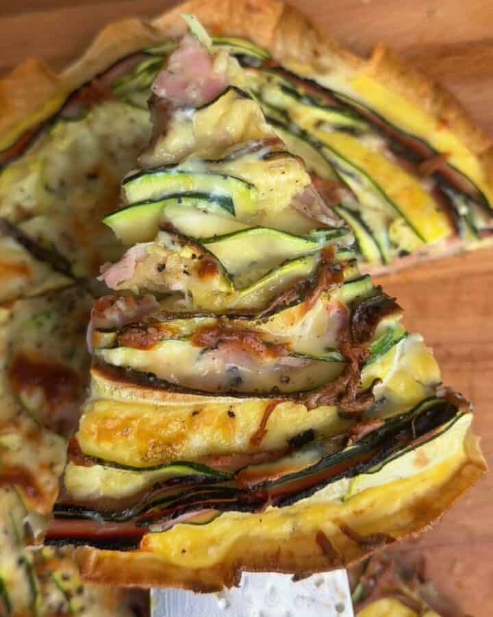 Slice of crispy zucchini and ham tortilla quiche with golden brown edges and melty cheese