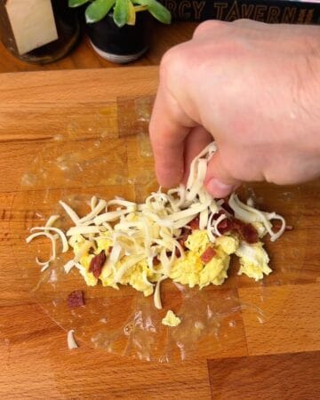 egg, bacon and shredded cheese on a rice paper sheet in prep for bacon egg and cheese rice paper bagel
