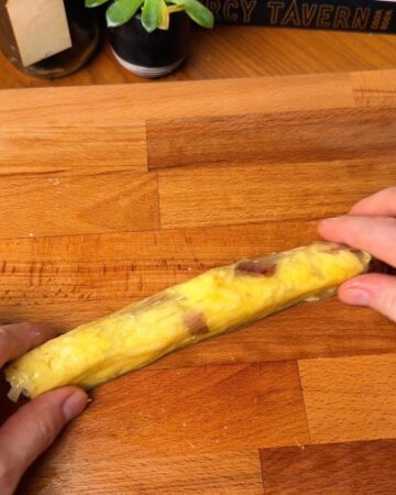 Hands rolling a rice paper sheet, filled with scrambled eggs, bacon, and shredded cheese in prep for a bacon, egg and cheese rice paper bagel
