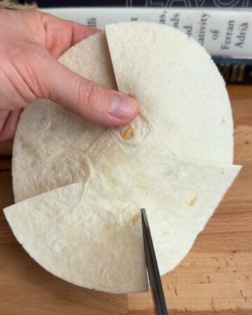 a tortilla being sliced in prep for the making of a bacon, egg, and cheese tortilla muffin