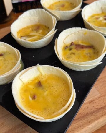 egg mixture of egg, bacon, and cheese in a tortilla in a muffin tin in prep for the making of a bacon, egg, and cheese tortilla muffin