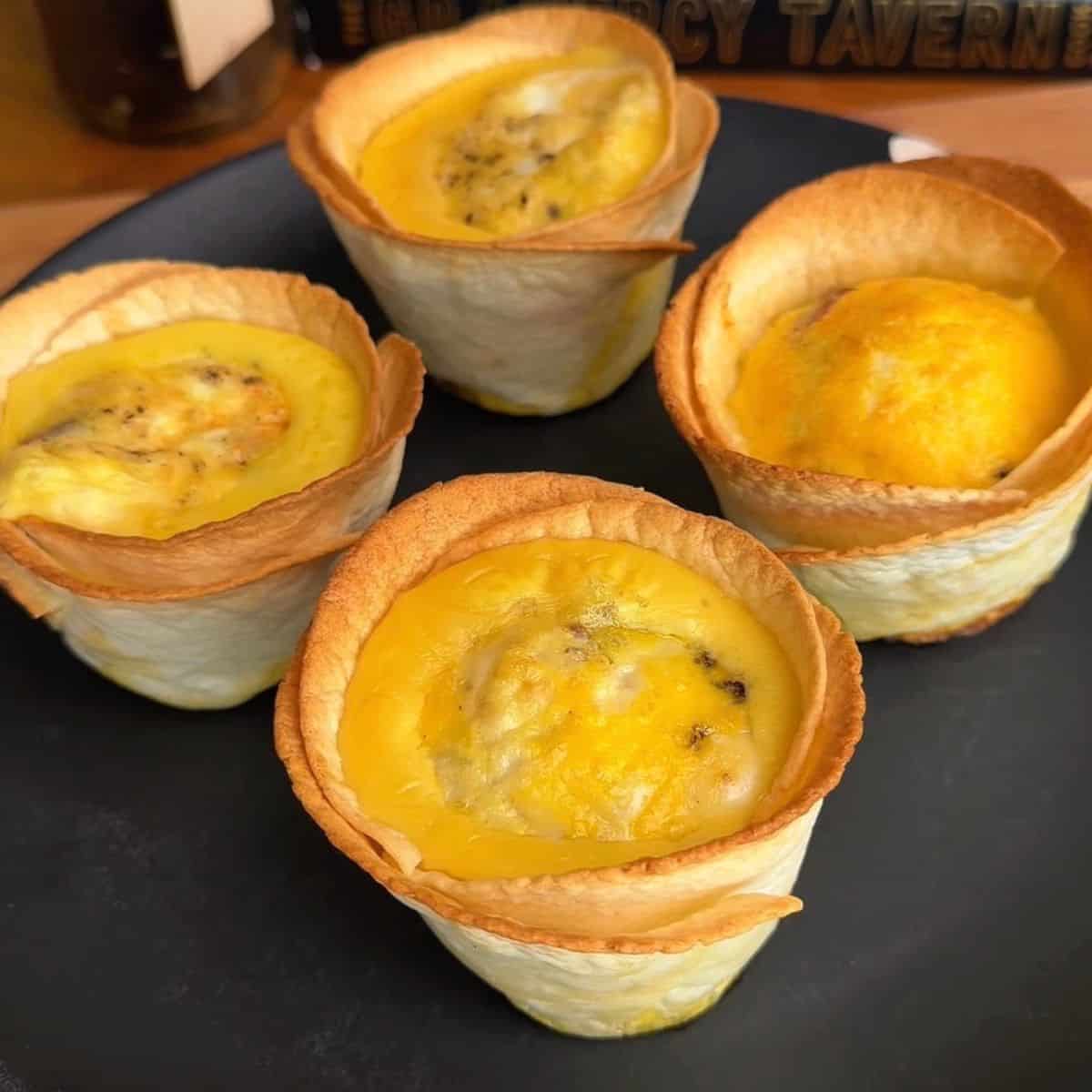 a plate of freshly baked bacon, egg and cheese tortilla muffins with crispy, golden brown edges and eggy centers