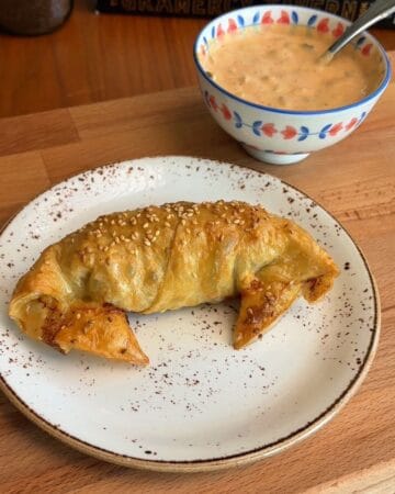 a finished, golden brown big mac rice paper croissant with punchy burger sauce on the side for dipping