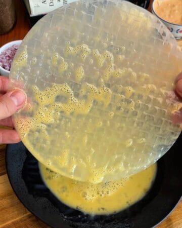 a rice paper sheet being dipped in egg wash for the making of a big mac rice paper croissant