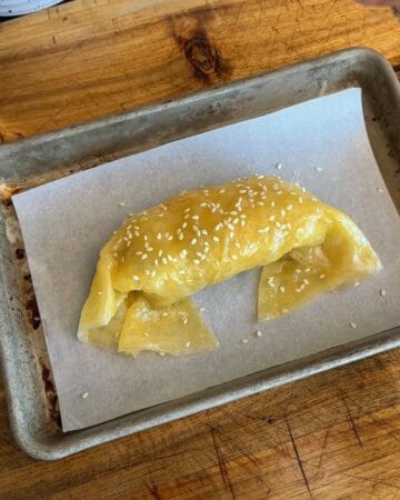 a rolled big mac rice paper croissant, sprinkled with sesame seeds, ready to go in the oven