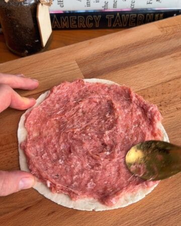 ground chicken being spread on a small tortilla in prep for the making of a crispy mcchicken smash taco