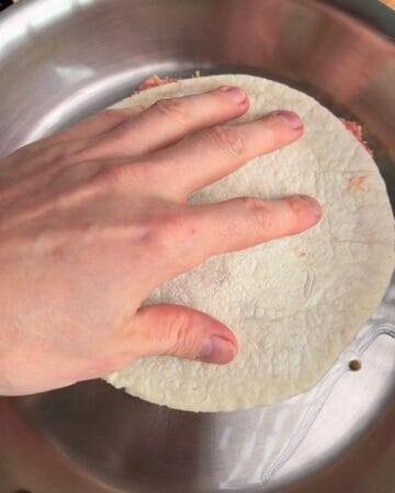 a tortilla, layered with ground chicken and bread crumbs, being smashed into an oiled pan for the making of a crispy mcchicken smash taco