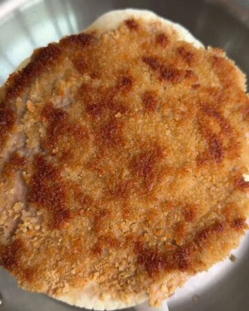 crispy chicken on a tortilla after being smashed in a pan, now ready for toppings, to finish the making of a crispy mcchicken smash taco