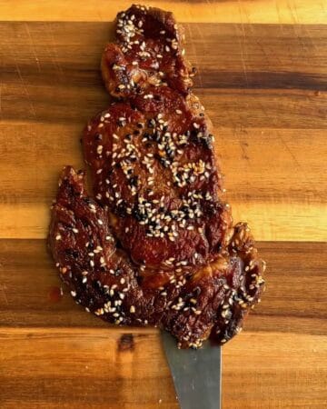 a crispy steak on a cutting board with black and white sesame seeds in prep for miso soy sesame steak over eggs
