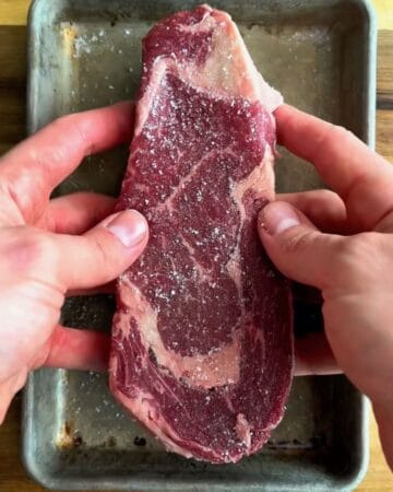 a steak being prepped with coarse salt in prep for miso soy sesame steak over eggs