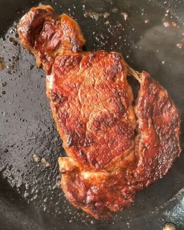 a juicy steak sizzling on a cast iron pan in prep for miso soy sesame steak over eggs