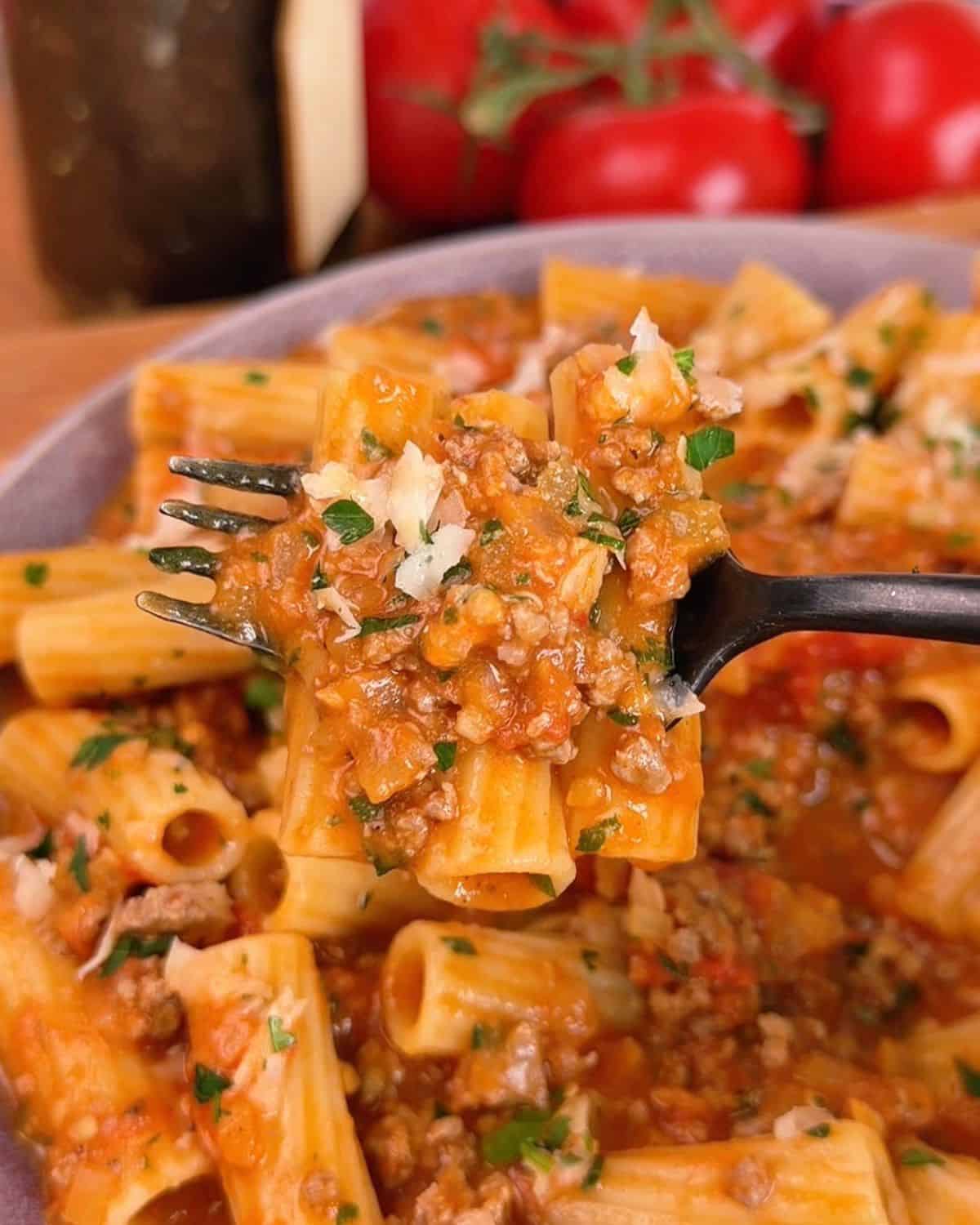 a bite of one-pan cheesy tomato beef rigatoni with shredded parmesan and parsley on top