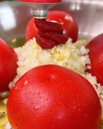 tomatoes blistering in a pan, with garlic, onion and tomato paste being added for the making of one-pan cheesy tomato beef rigatoni with shredded parmesan and parsley on top