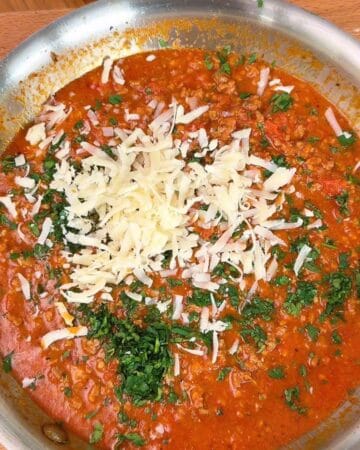 Delicious beef sauce topped with shredded cheese and fresh herbs, served in a metal bowl.