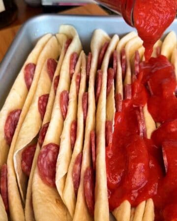 tomato sauce being layered in the cracks of accordion style folded tortillas in prep for tortilla pull apart pizza bread