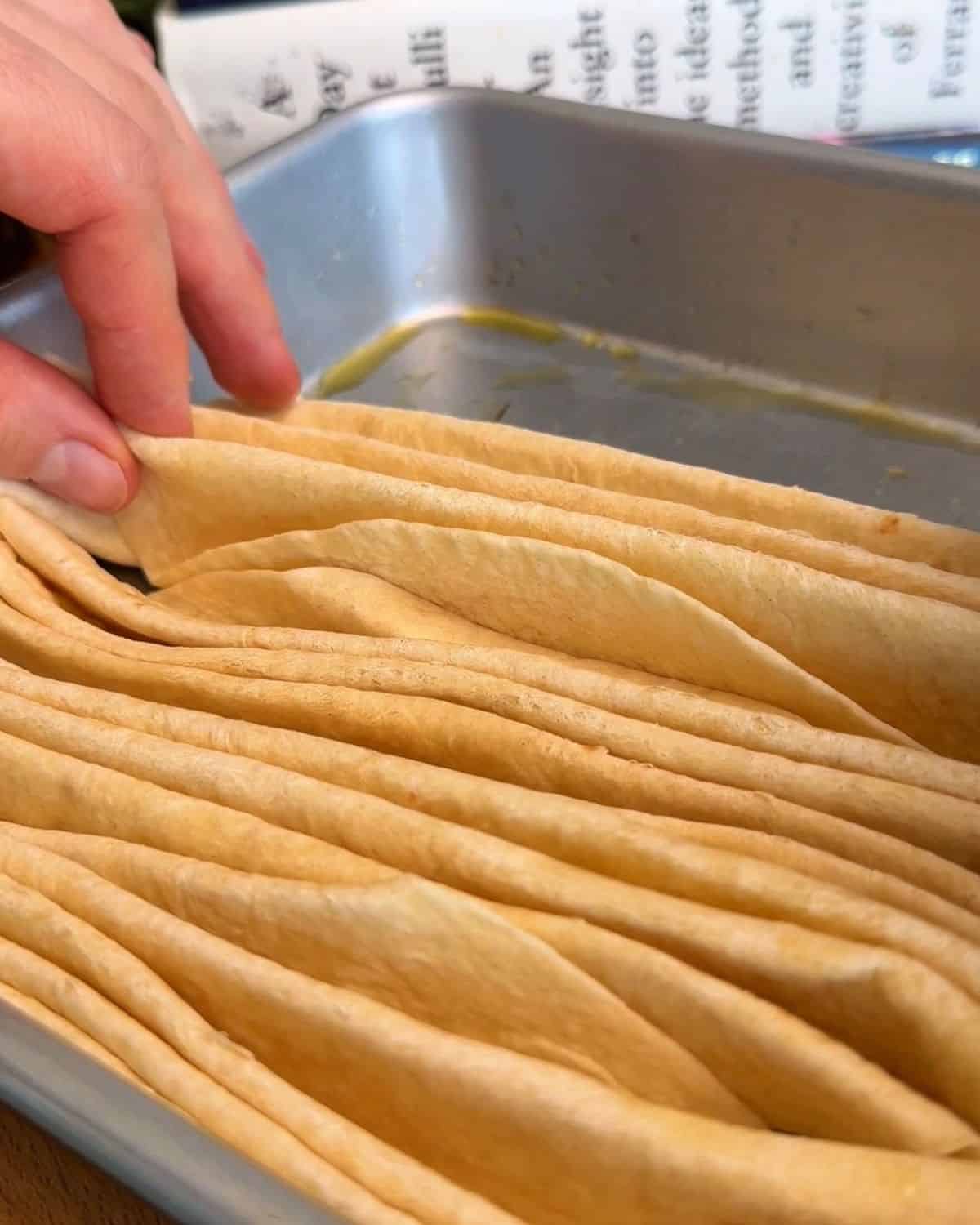 accordion folded tortillas stacked in a baking dish in prep for crispy, cheesy, tortilla pull apart pizza bread