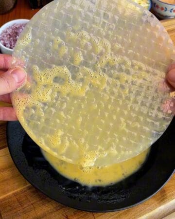 rice paper sheet being dipped in egg wash in prep for a big mac rice paper spiral