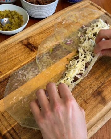 ground beef, onion, and shredded cheese being rolled into rice paper sheets for a rice paper big mac spiral