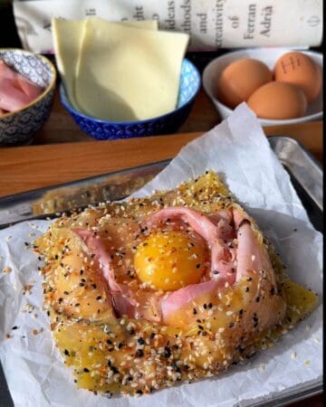 a rice paper croque madam ready to go on the oven, sprinkled with everything bagel seasoning and an egg on top